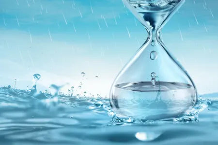 A clear glass hourglass filled with water, under a blue rainy sky.